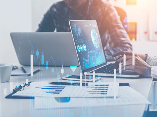 Business people working with laptops in blurred office with double exposure of business infographics and graphs