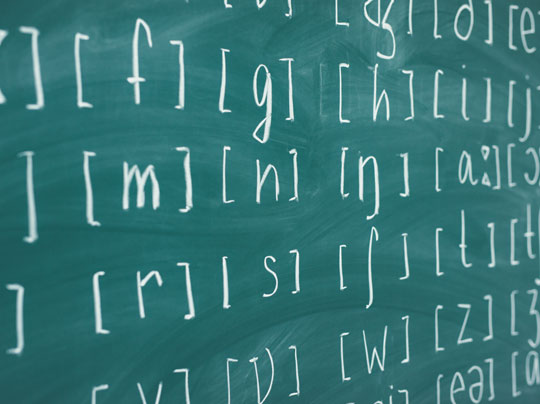 A green chalkboard with letters, symbols, and markings represent Linguistics programs at Boston University.