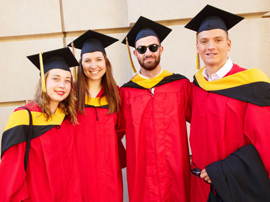 A photo of four recent BU MET graduates outside Agganis Arena on Commonwealth Avenue in Boston before commencement.