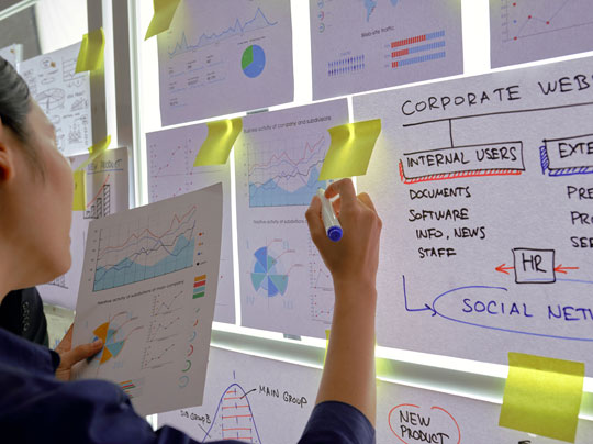 A marketing student mapping out a flow chart with yellow sticky notes on a lighted wall-mounted display board.