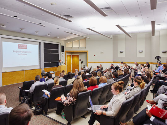 Business students listening to a professor discuss Project Management in Practices in a full classroom at Boston University.