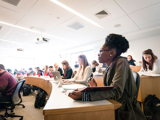 Students in a theater style classroom looking intently across a Boston University classroom at a presenter.