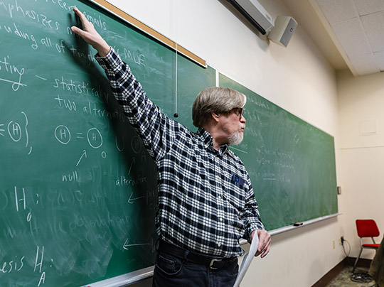 A BU MET professor teaching an Actuarial Science class; reviewing notes on a chalkboard