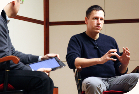 Entrepreneur seated and speaking on stage to a crowd