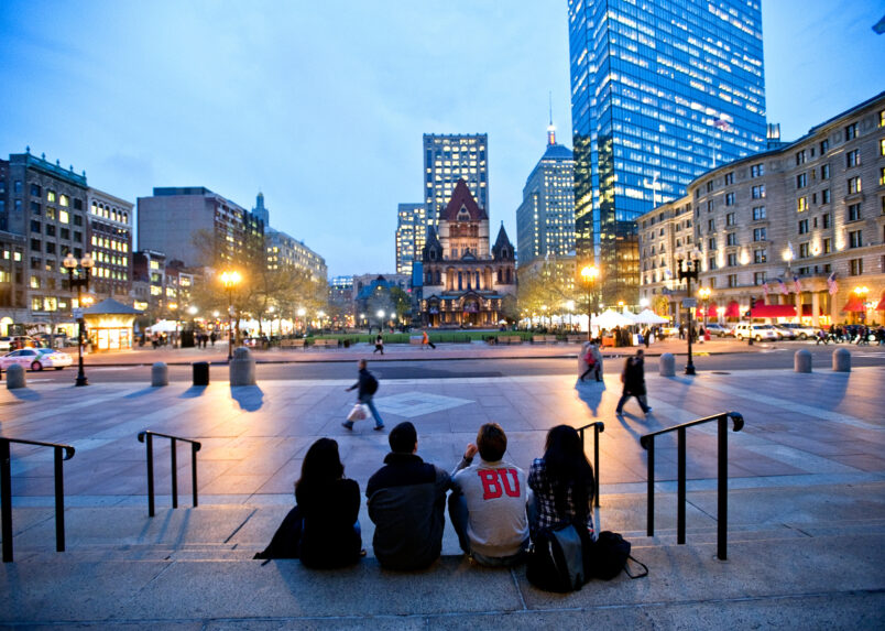 Four students sit on the steps of the Boston Public Library looking out onto Copley Square