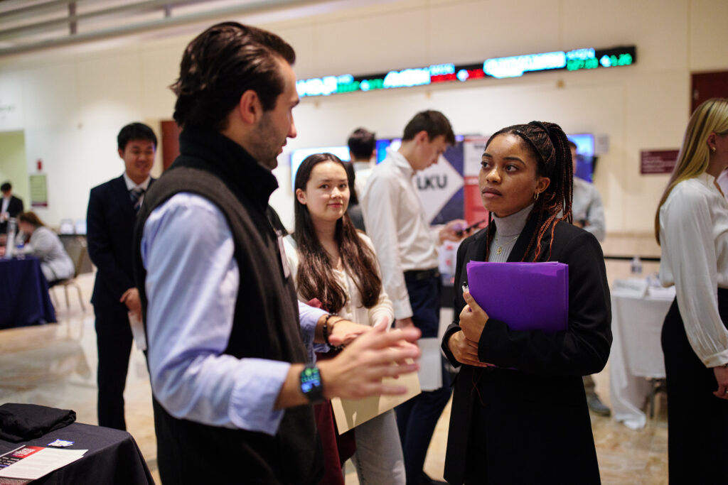 Female student holding a binder speaking with a male recruiter at a recruitment fair.