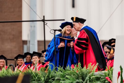 Dean Fournier listening to a professor whisper something to her on stage at graduation