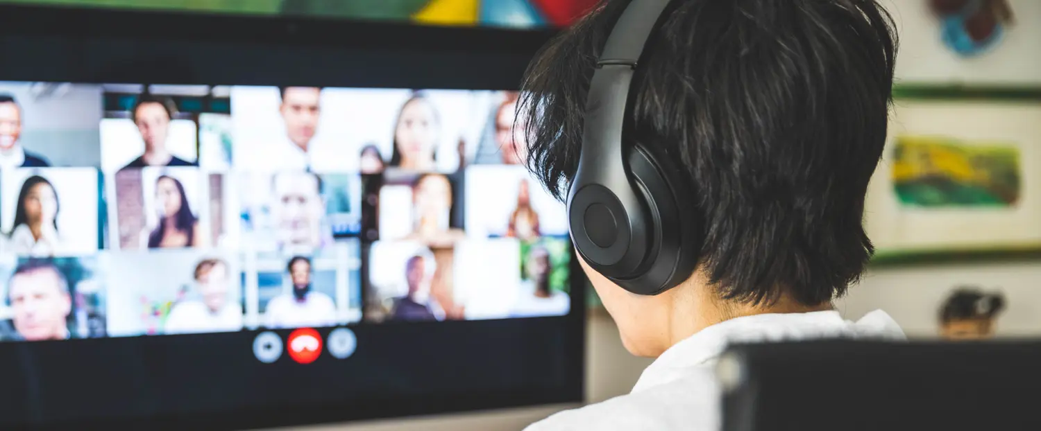 Student with short dark hair and headphone facing an online Zoom classroom