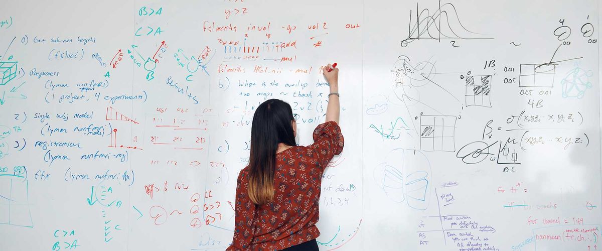 A person stands in front of a white board the person has long dark hair