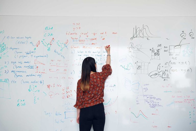A person stands in front of a white board the person has long dark hair