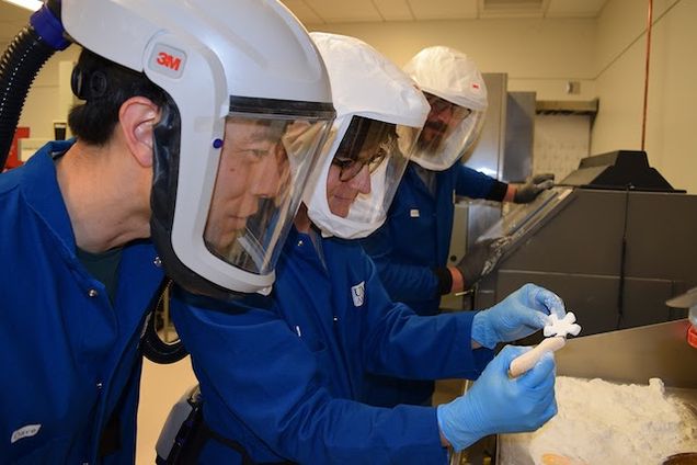 Three researchers studying objects while wearing PPE