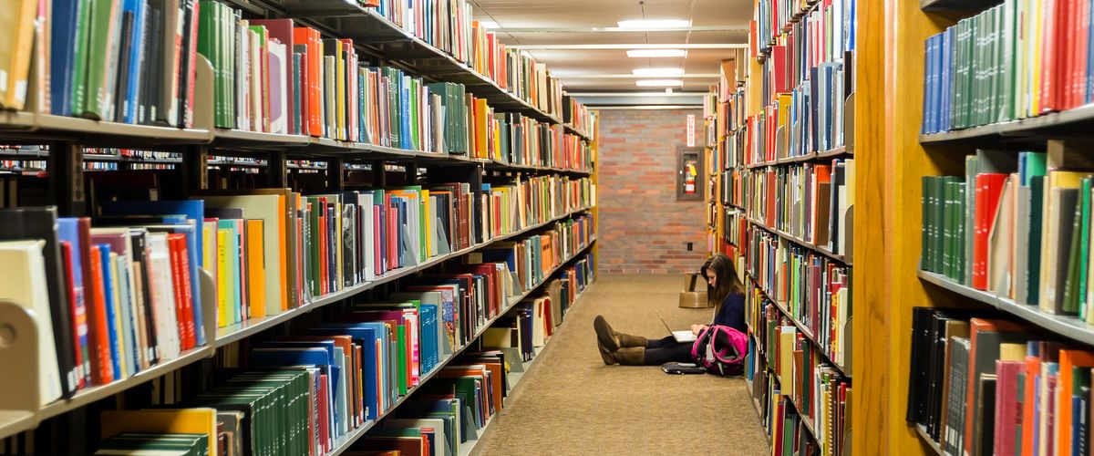 A woman sitting on the floor in the library, reading a book