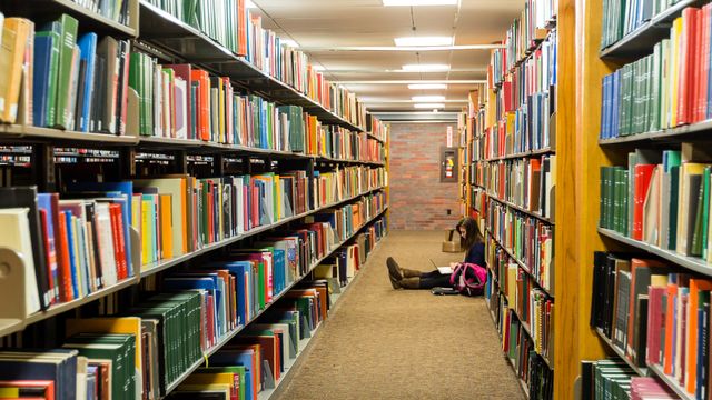 A woman sitting on the floor in the library, reading a book