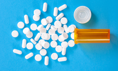 prescription bottle of oxycodone and hydrocodone pills spilled on a blue background 