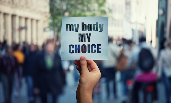 Feminist hands holding a protest banner with the message my body my choice over a crowded street