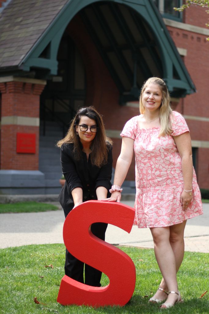 Rea Shqepa and Ashley Leonard standing with a large letter S in front of the Talbot Building