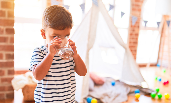 Toddler boy drinking glass of water at kindergarten