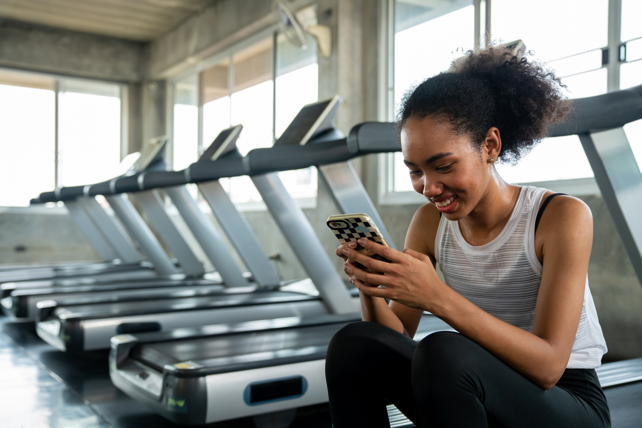 Black athletic woman using mobile phone while exercising at fitness gym.