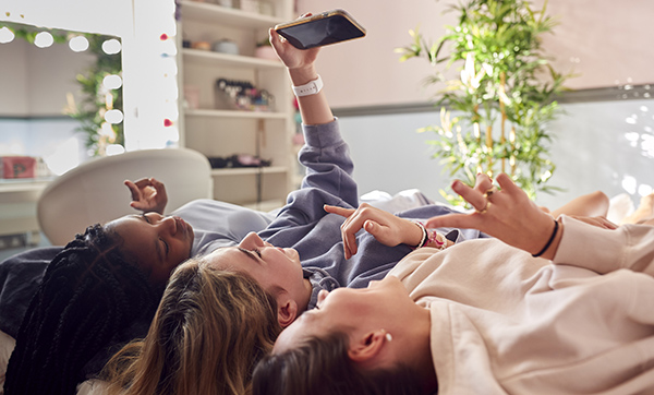 Group Of Smiling Multi-Cultural Teenage Girl Friends Posing For Selfie On Mobile Phone At Home