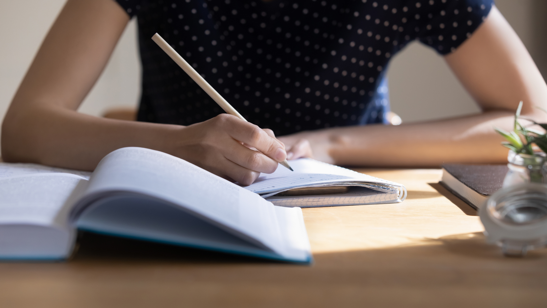 Young student girl preparing for college test, exam, writing notes, making draft, summary of textbook, studying, reading book for class report. Learning workplace table close up, banner shot