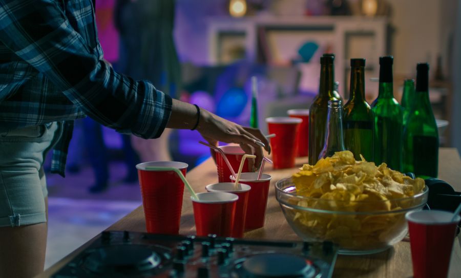 At the College House Party: Girl Takes Glass with Drink from the Tray. Diverse Group of Friends Have Fun, Dancing and Socializing. Disco Neon Strobe Lights Illuminating Room.