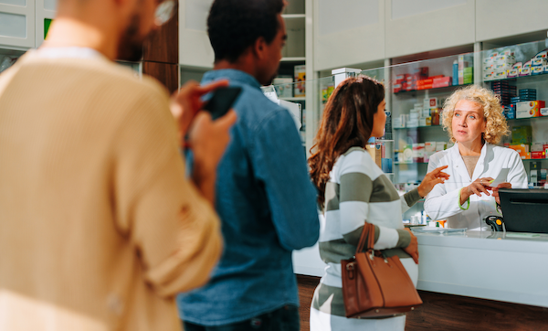 A number of people are in the pharmacy, standing in line behind a pregnant woman.