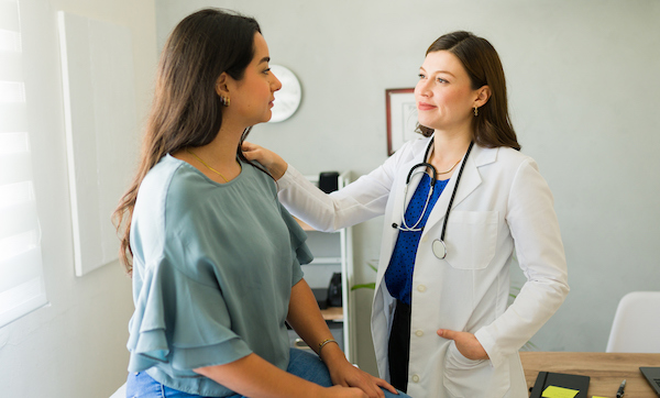 Woman doctor offers comfort to her patient by placing a hand on her shoulder during a diagnosis discussion in the doctor's office