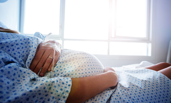Close-up of a pregnant woman's belly in the hospital bed with catheter in hand