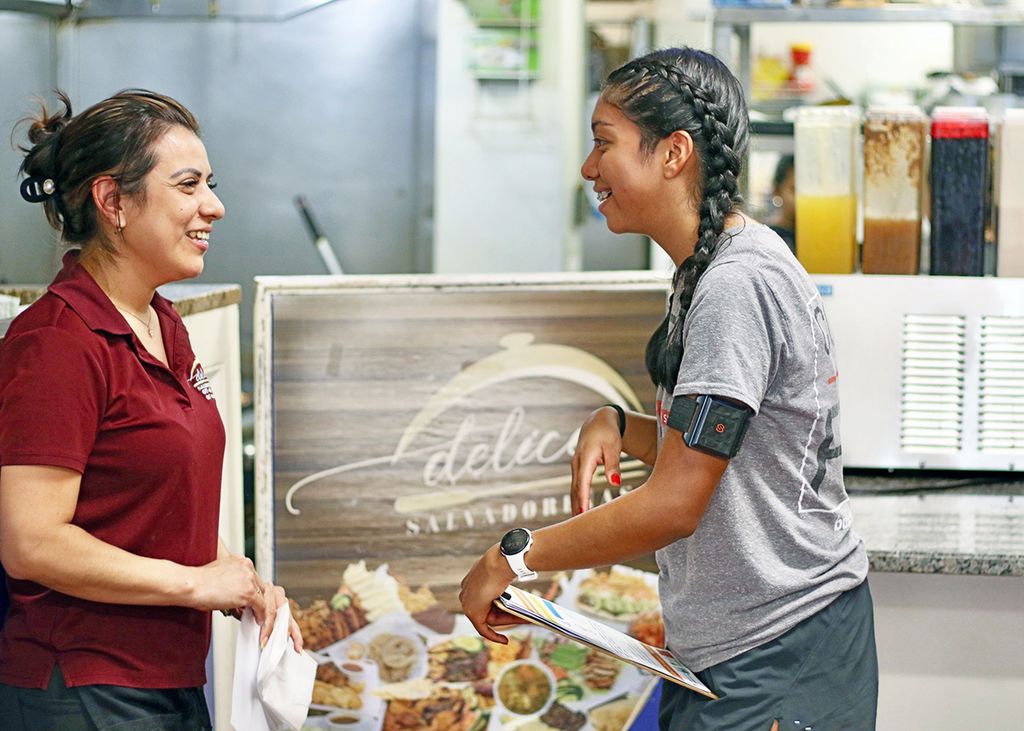 Victoria A. Lopez (right), an MPH student, explains how the wearable temperature sensor on her left arm works to a potential study participant at a restaurant in Chelsea.