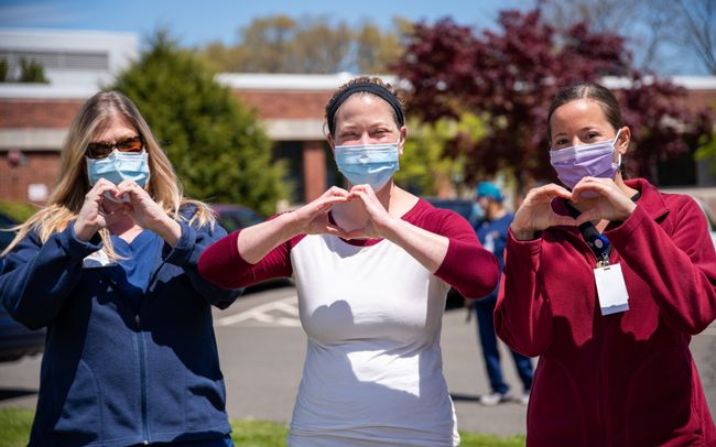 3 professionals wearing masks make a heart with their hands