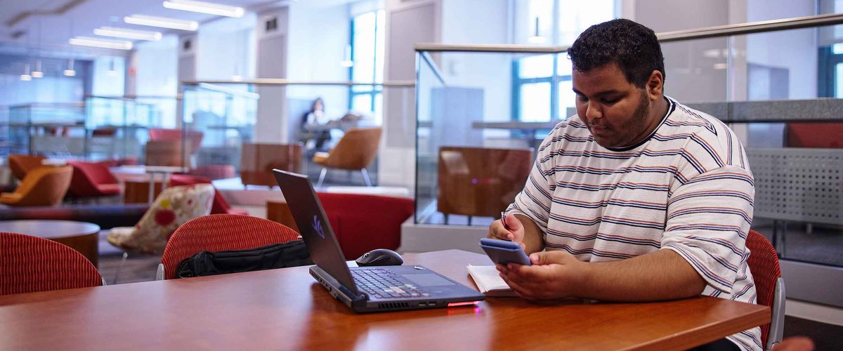 A student workin on his computer at a library on BU's campus