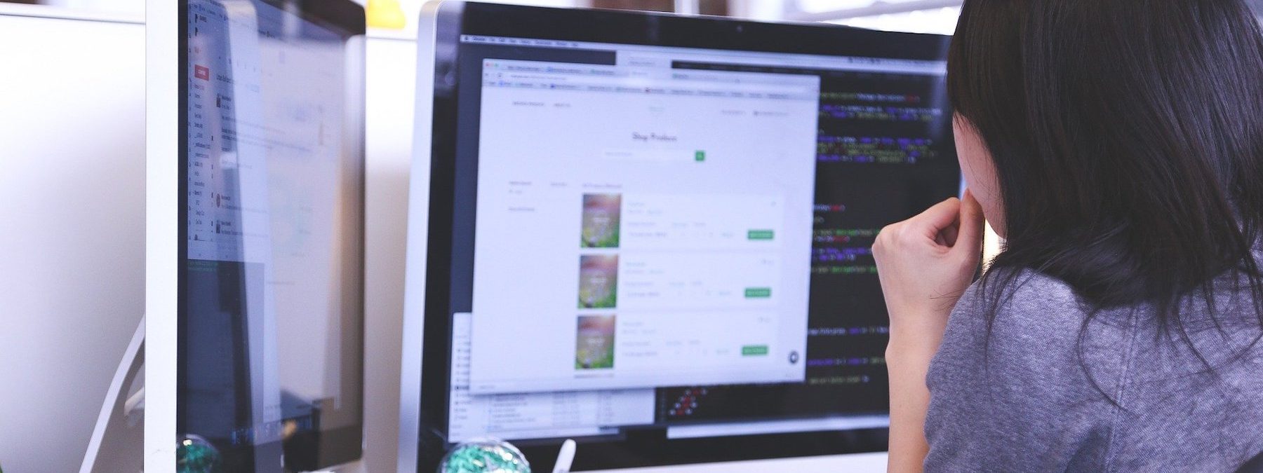 Woman sitting in front of a dual monitor desktop, looking at the screens