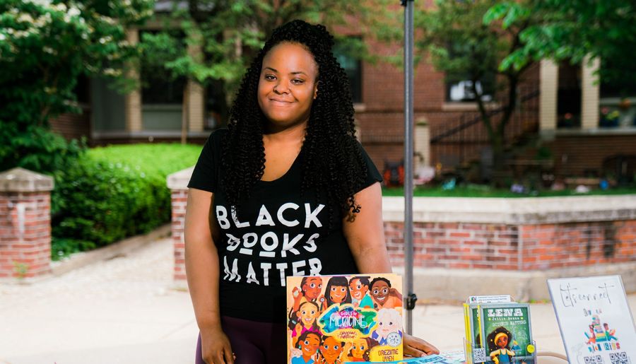 Black women wearing black lives matter t shirt stand behind a table with children's books