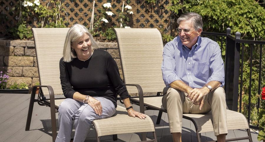 Older couple sit laughing on lounge chairs in backyard
