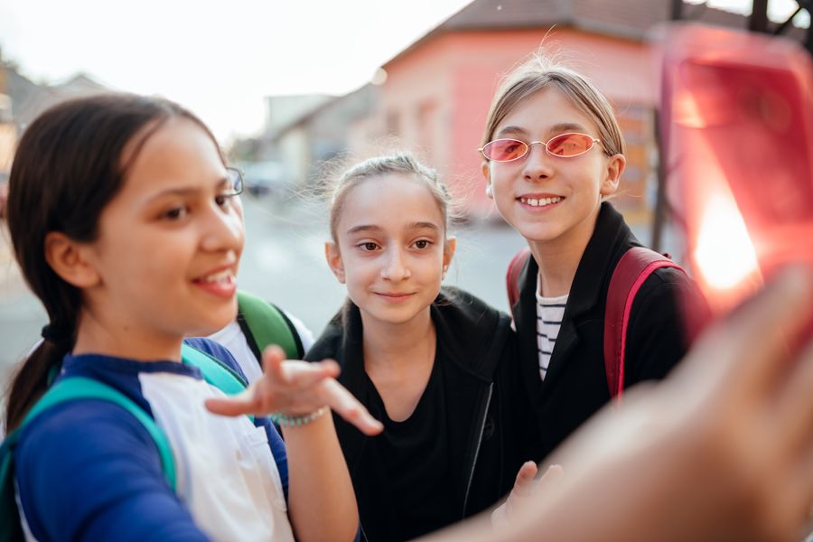 Three middle school aged girls smiling looking at phone