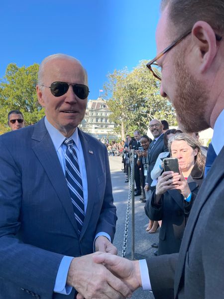 President Joe Biden on the left in sunglasses reaching hand out to shake the hands oof Josh Goodman