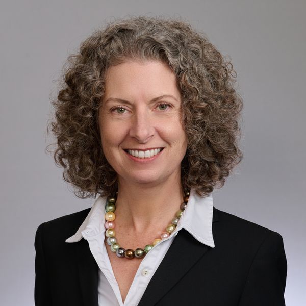 Shows Penny Bishop, who has short curly hair and is wearing a white collared shirt and black jacket