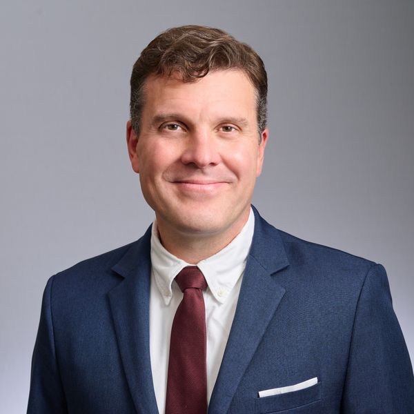 Shows Todd Czubek, who has short brown hair and is wearing a red tie, a white shirt, and a blue suit jacket