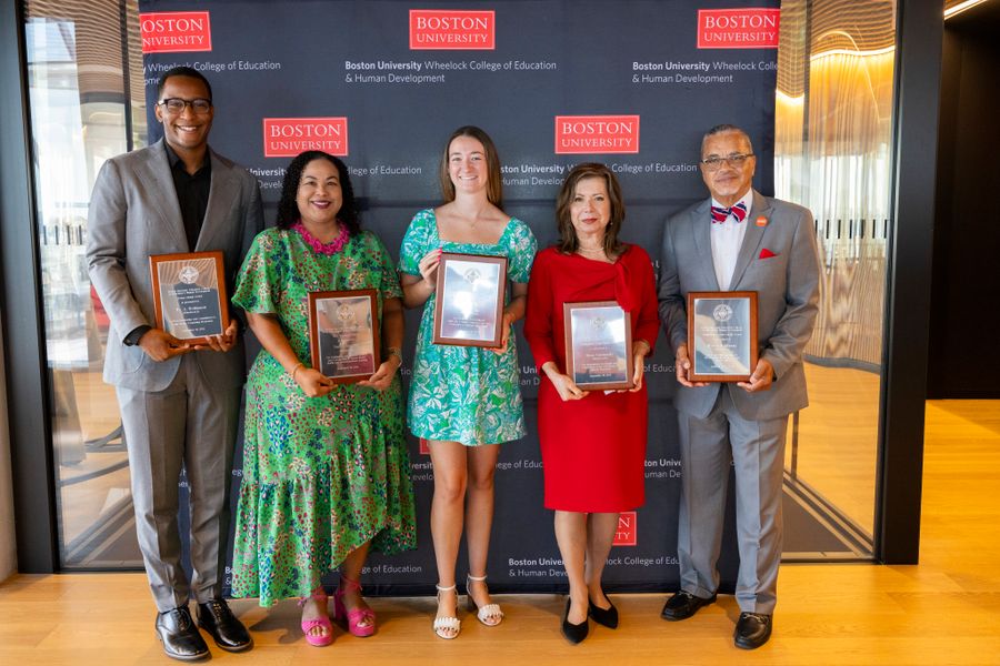 The five alumni award winners standing with their awards infront of a black step and repeat reading Boston University Wheelock College