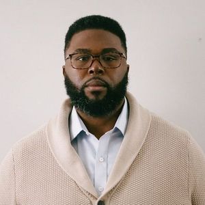 Shows Anthony Jack wearing an off white cardigan over a white collared shirt