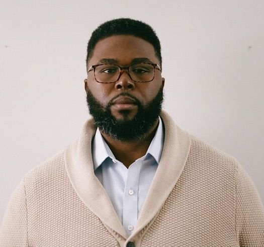 Shows Anthony Jack wearing an off white cardigan over a white collared shirt
