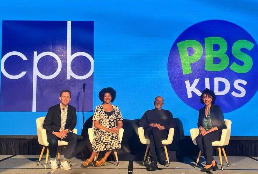 Shows four people sitting on a stage in front of a sign that says CPB and PBS KIDS