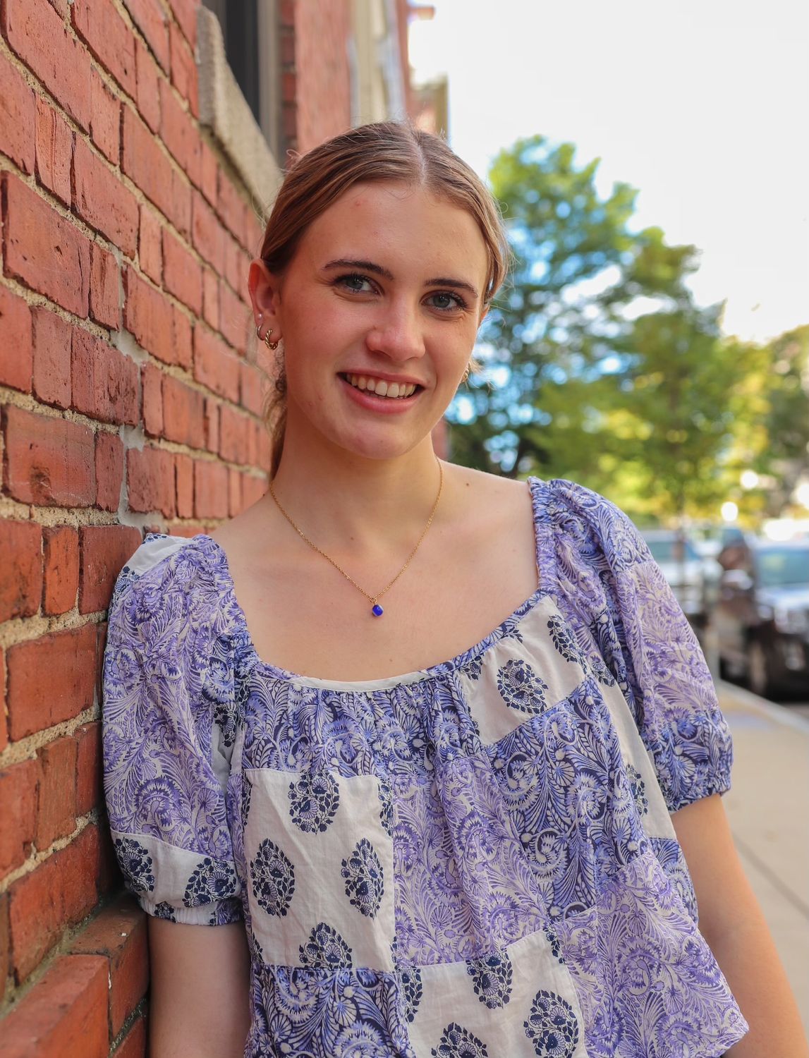 Female student leaning against brick wall smiling on Boston street