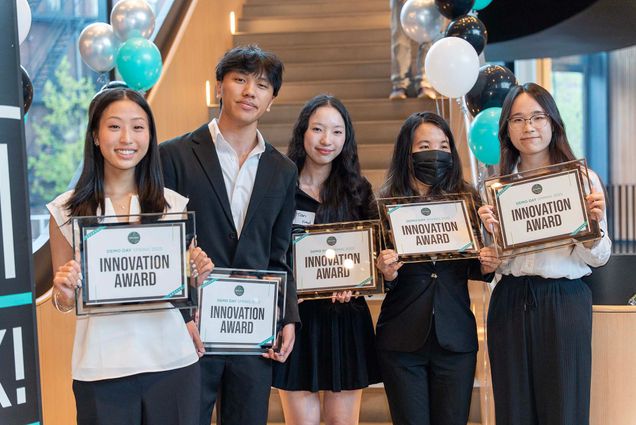 Five students stand smiling and holding framed certificates labeled “Innovation Award” at BU Spark! Demo Day Spring 2025. They are dressed in business or semi-formal attire, and balloons decorate the staircase behind them.