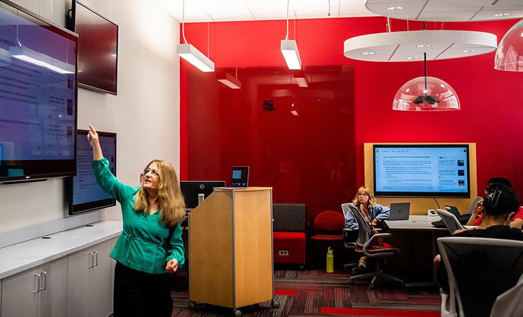 Margaret Wallace points to a screen while seated students look on.