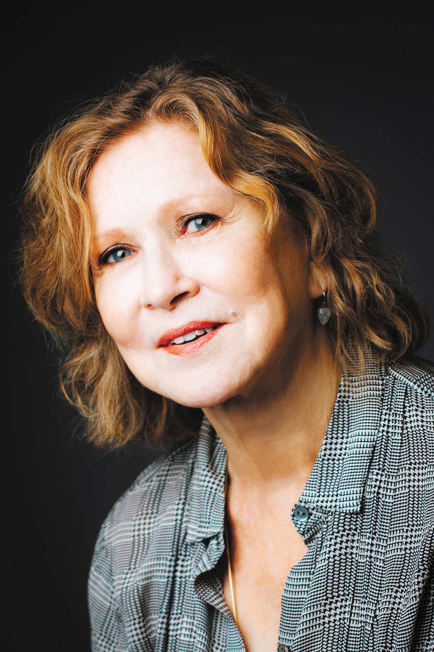 Portrait of Best-selling author and BU alum Sue Miller on a black background. She smiles slightly and wears a black and white stripped shirt.
