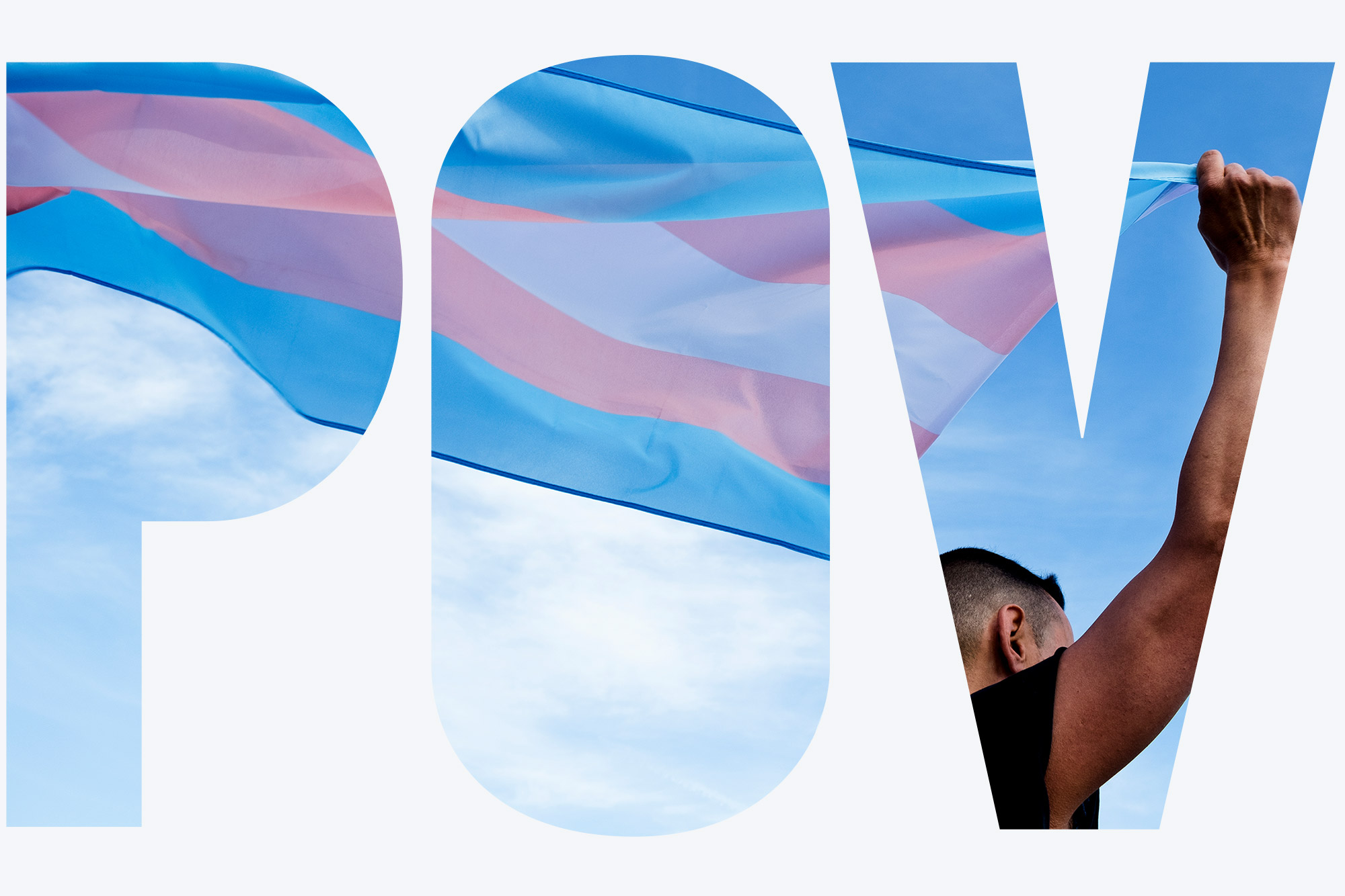 Photo of a masculine person holding a trans pride flag behind their shoulders. The sky is blue with a few clouds.