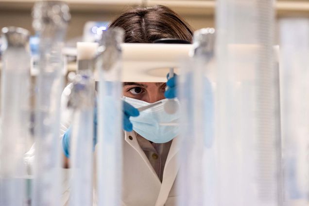Closeup photo of undergrad researcher Halle Cooper (CAS’22) measures the absorption spectra of suspended particles in water samples collected from Louisiana wetlands. In the foreground are a series of plastic vials. Cooper is seen wearing a mask and looking very concentrated as she uses tweezers while taking measurements.