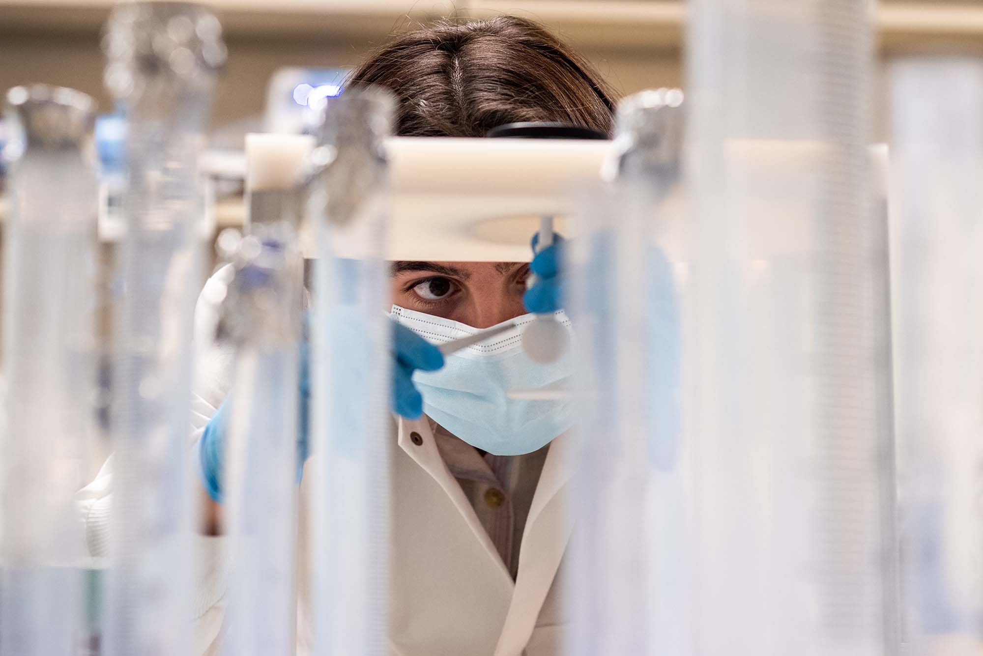 Closeup photo of undergrad researcher Halle Cooper (CAS’22) measures the absorption spectra of suspended particles in water samples collected from Louisiana wetlands. In the foreground are a series of plastic vials. Cooper is seen wearing a mask and looking very concentrated as she uses tweezers while taking measurements.