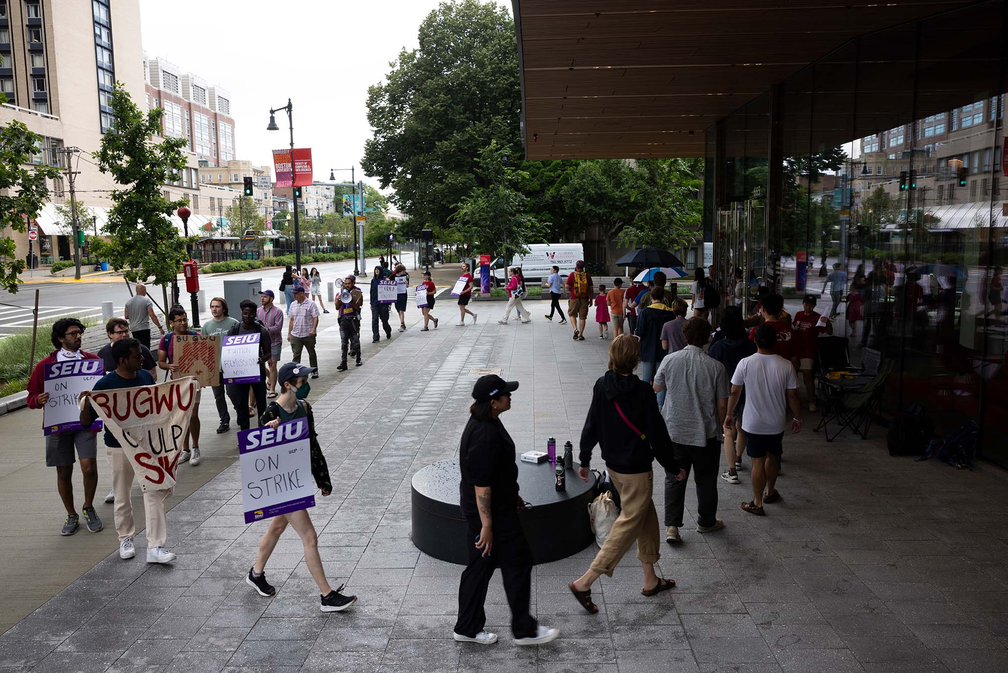 Photo: A picture of a strike on Boston University's campus. It features members of the BU Graduate Workers Union and community members supporting them in front of a modern academic building